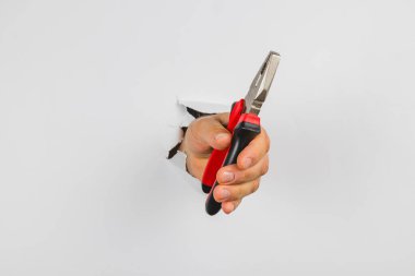 Beyaz bir duvardaki delikten bir el çıkıyor, penseyi sıkıca kavrıyor. Bu sahne, aracın detaylarını vurgulayarak şaşırtıcı bir an sergiliyor.