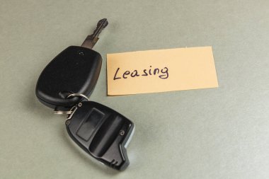 Siyah kumandalı bir araba anahtarı sade bir arka planda durur. Anahtarların yanında kira sözleşmesini işaret eden elle yazılmış bir etiket var..