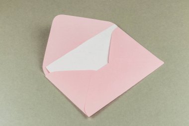 Açık gri bir yüzeyde açık pembe bir zarf, içine bir mektup ya da kart konmasını bekliyor. Temiz tasarımı basitliği ve zarafeti vurgular..
