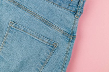 Light blue denim jeans laid flat on a pink background display stitching and pocket design that highlights the fabric's texture and color contrast.