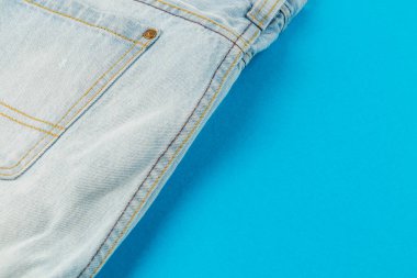 Light blue denim jeans are displayed against a bright blue background, showcasing their texture and design details. This simple arrangement highlights casual fashion.