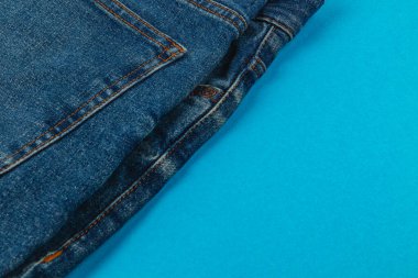 Blue jeans are folded and arranged on a bright blue surface, showcasing their texture and color in a visually appealing way.