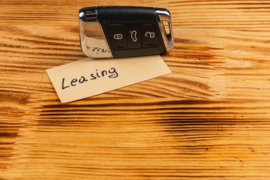 A car key is resting on a wooden surface next to a note that says Leasing. The setup suggests a focus on leasing vehicles or rental agreements.