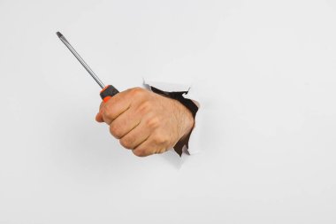 Bir el, beyaz bir duvarın yırtık bir bölümünden uzanıp tornavidayı tutuyor. Bu da bir evde onarım ya da bakım yapılmasını önerir..