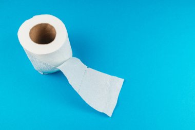 Bir rulo yumuşak banyo dokusu canlı mavi bir yüzeye oturur. Doku, yumuşak dokusunu ve tasarımını gözler önüne seriyor..