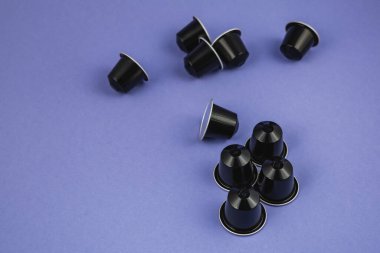 Lviv Ukrayna 12.08.2025 birkaç siyah kahve kapsülü açık mor bir yüzeye saçılmıştır. Bazı kapsüller diktir, bazıları ise uzanır..