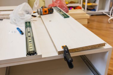 Lviv Ukrayna 12.10.2025 Bir kişi marangozluk projesi üzerinde çalışıyor. Matkap ve kıskaç gibi araçlar atölye ortamında montaj için hazırlanmış tahta tahtalarla bir tezgahın üzerine yerleştirilir..