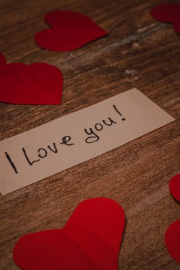 Kırmızı kağıt kalpler ahşap bir masanın etrafını sarar. Notta basit bir aşk mesajı var. Sahne, özen ve sıcaklığın doğrudan dışavurumunu gösteriyor..