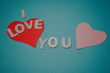 Kırmızı ve pembe kalpler, seni seviyorum kelimelerini çevreleyen mavi arkaplandaki kesik harflerle basit bir sevgi ve özen ifadesi gösteriyorsun..