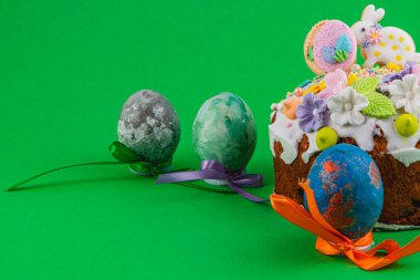 Renkli yumurtalar ve süslemeli bir pasta birlikte düzenlenir. Sahne, canlı detaylarla dolu bir Paskalya kutlaması için uygun renkleri gösteriyor..