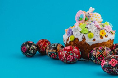 Süslü yumurtalarla çevrili mavi bir yüzeye renkli bir pasta yerleştirilir. Pastada çiçekler ve Paskalya sembolleri gibi şenlikli bir atmosfer gösteren süsler var..