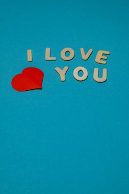 Mektuplar açık mavi bir yüzeyde aşk mesajı yazar. Kırmızı kalp grafiği basit zanaat görünümüne renkli bir element ekler.