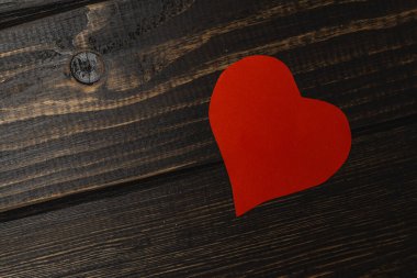 Kağıttan yapılmış kırmızı bir kalp, siyah bir ahşap masanın üzerinde duruyor. Tahtanın dokusunu gösteren bir tahıl deseni var. Sahne basit ve doğrudan..