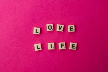 Kiremitler Ulusal Scrabble Günü münasebetiyle pembe bir zeminde aşk ve hayat kelimelerini gösteriyor. İnsanlar bu özel günde oyunları sever ve kelimelerle iletişim kurarlar..