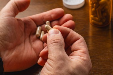 Bir insan, diğer kapsüller avuçlarında dinlenirken bir elini destek kapsülü olarak kullanır. Masanın yanında bir şişe kapsül var..