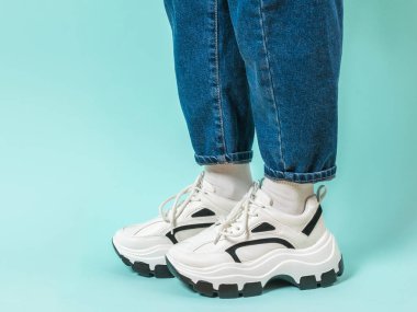 Geniş kot pantolon ve beyaz spor ayakkabı giyen şık giyimli bir çocuğun bacakları. Şık gençlik kıyafetleri ve ayakkabıları. Metin için yer.