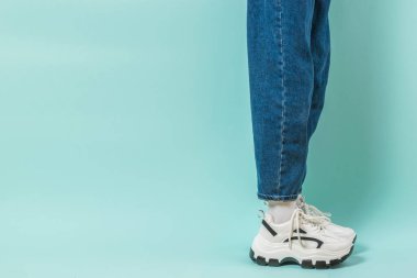 Geniş kot pantolonlu ve yüksek tabanlı spor ayakkabılı kızın bacağının yan görüntüsü. Metin için yer.