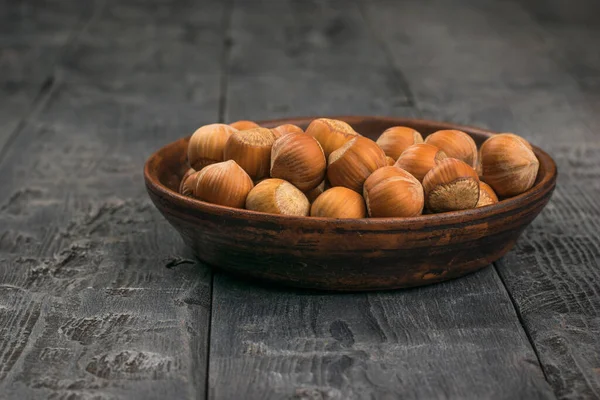 Φουντούκια στα κοχύλια τους σε πήλινο κύπελλο σε ξύλινο τραπέζι. — Φωτογραφία Αρχείου