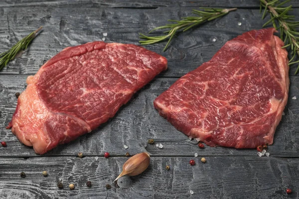 Dois bifes, alecrim e alho em uma mesa de madeira. — Fotografia de Stock