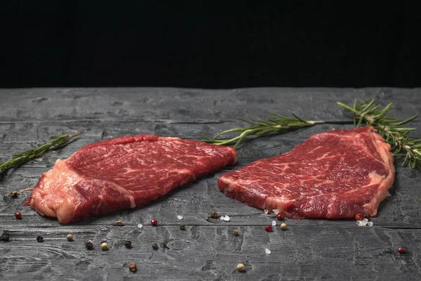 Dva hovězí steaky s bylinkami na černém dřevěném stole. — Stock fotografie