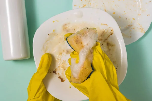 Hands in rubber gloves wash the dishes with a foam sponge.