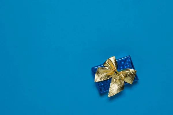Blue box with a gift in a gold ribbon on a blue background. — Stock Photo, Image