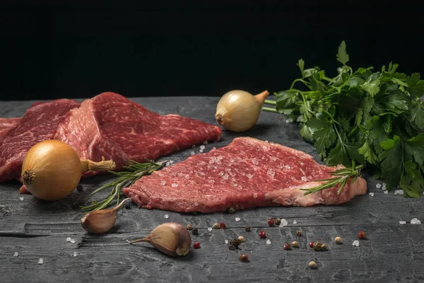 木のテーブルの上にニンニクのクローブ、玉ねぎ、新鮮な牛肉のステーキ. — ストック写真