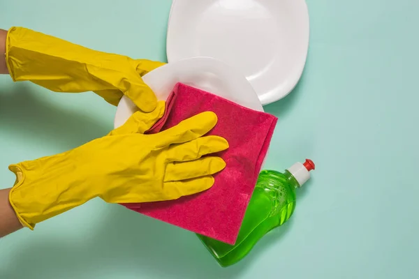 Hands in rubber gloves wipe clean dishes with a red cloth.