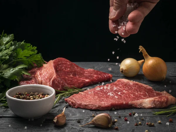 A mão de um homem polvilha grande sal marinho em bifes de carne. — Fotografia de Stock