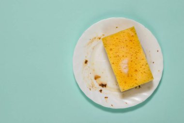 Kirli beyaz tabak ve sünger. Mavi arka planda temizlik jeli..