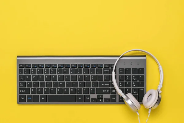Trådlöst tangentbord och vita hörlurar på en gul bakgrund. Utsikten uppifrån. — Stockfoto