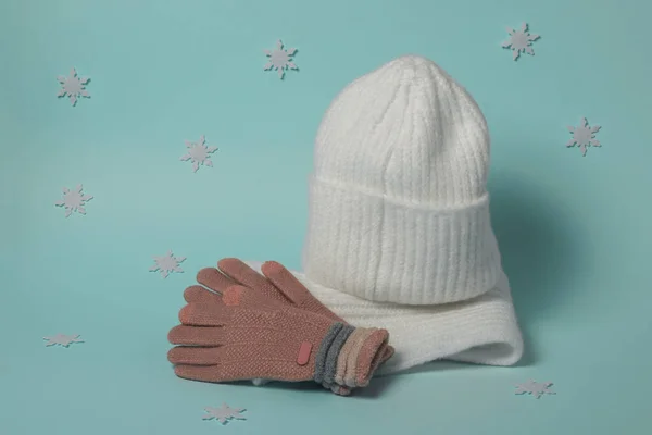 Gestrickte Handschuhe, Mütze und Schal auf blauem Hintergrund mit Schneeflocken. — Stockfoto