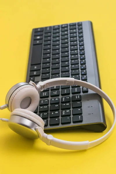Класична бездротова клавіатура та білі навушники на жовтому фоні . — стокове фото