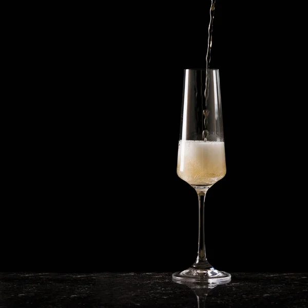 Llenar una copa con champán sobre un fondo negro. — Foto de Stock