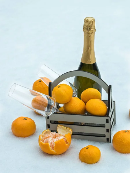 Eine Flasche Champagner, eine Schachtel Mandarinen und Gläser im Schnee. — Stockfoto