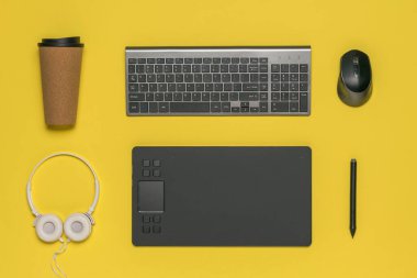 Kahve fincanı, klavye, fare ve grafik tableti sarı arka planda.