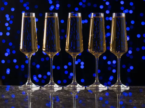 Cinco copos de vinho em pé ordenadamente sobre a mesa contra um fundo azul bokeh. — Fotografia de Stock