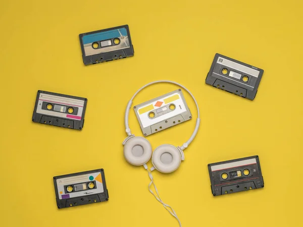 Białe słuchawki na tle rozrzuconych kaset na żółtym tle. — Zdjęcie stockowe
