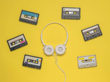 Sarı arka planda altı teyp ve beyaz kulaklık. Klasik ses kayıt depolama ve çalma araçları.