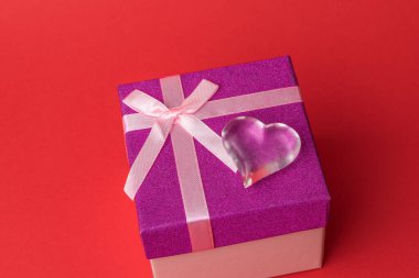 Kırmızı arka plandaki hediye kutusunda cam kalp. Bir aşk ilanı.