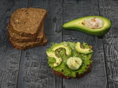 Yarım avokado, salatalıklı ekmek ve tahta masada salata. Sağlıklı beslenme.