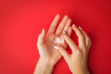 Çocukların elleri, kırmızı arka planda cam bir kalbi nazikçe tutuyor. Aşkın ve yaşamın sembolü..