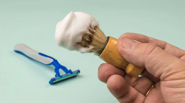 Shaving brush with shaving foam in the hands of a man on a light background. Set for care of a man\'s face.