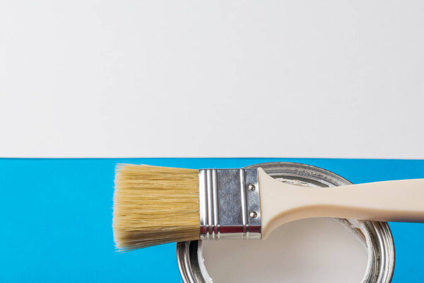 Банка белой краски и кисть на границе двух цветов. Выполнение живописных работ.