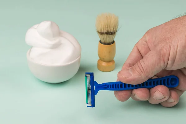 A man with a disposable razor on a background of foam and shaving brush. Set for care of a man's face.