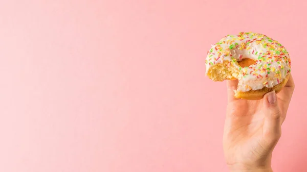 Hand of a girl with a bitten donut on a pink background. Popular pastries.