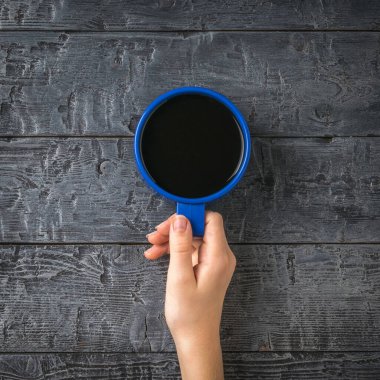 Tahta bir masada bir fincan kahve tutan bir el. Popüler canlandırıcı bir içecekle bir kadın eli..