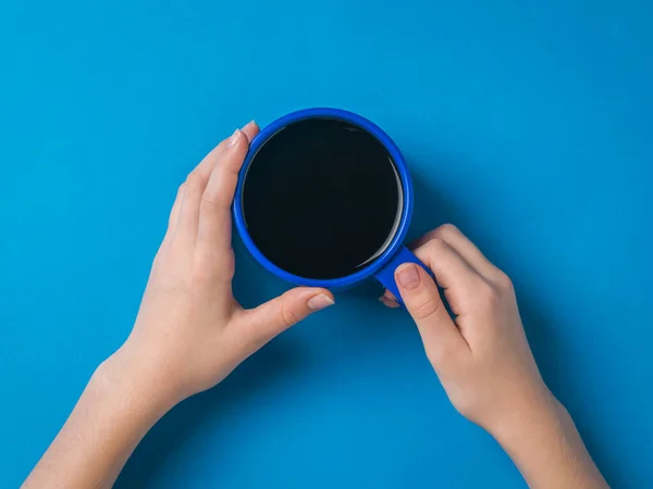 A girl with a bright blue coffee mug in her hands on a blue background. A woman's hand with a popular invigorating drink.