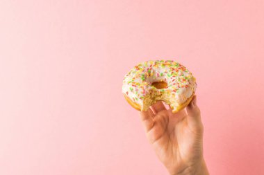 Açık pembe arka planda kemirilmiş donutla bir çocuk eli. Popüler hamur işleri.