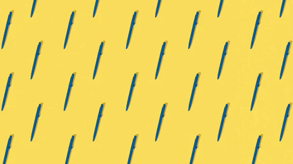 A pattern of blue ballpoint pens on a yellow background. Office supplies.